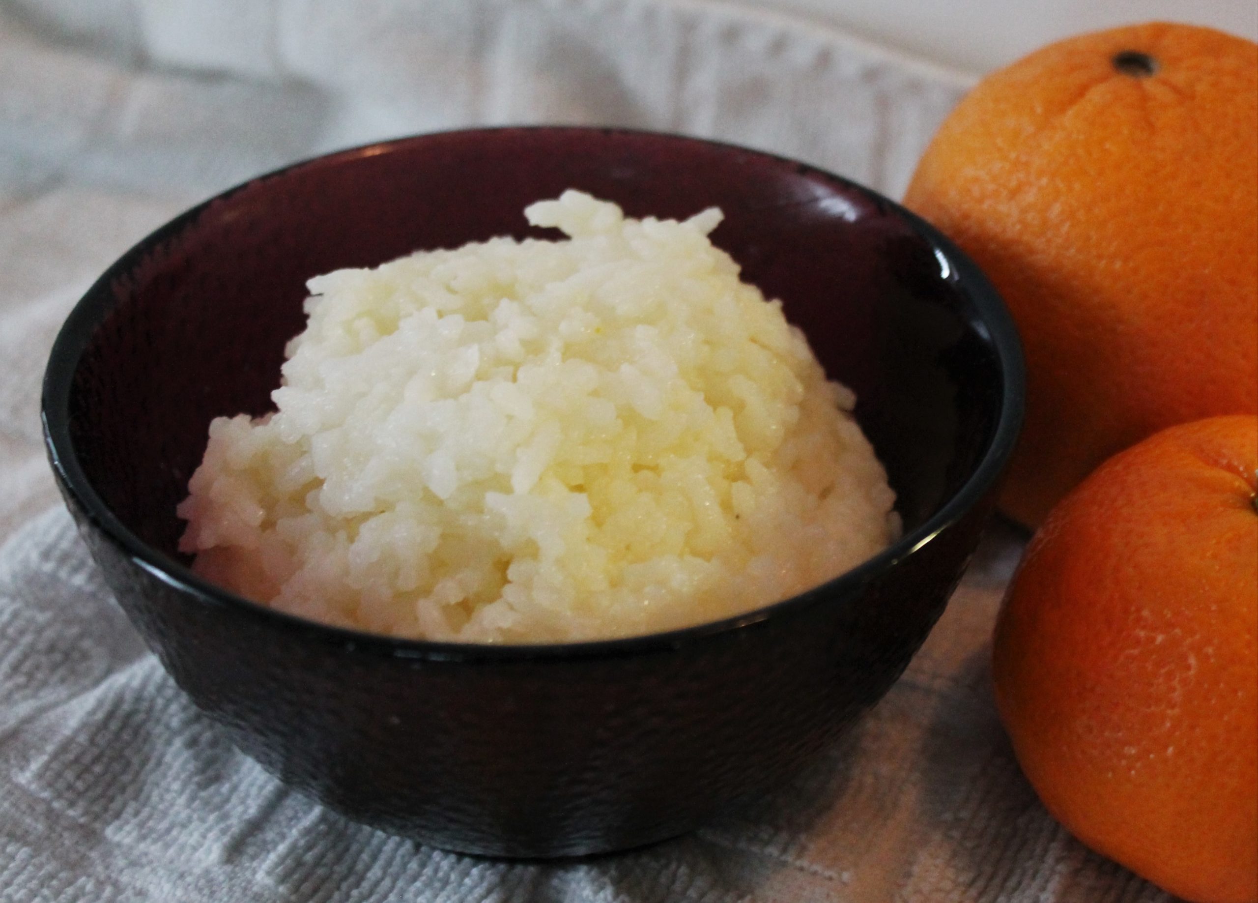 bowl of orange rice next to two oranges